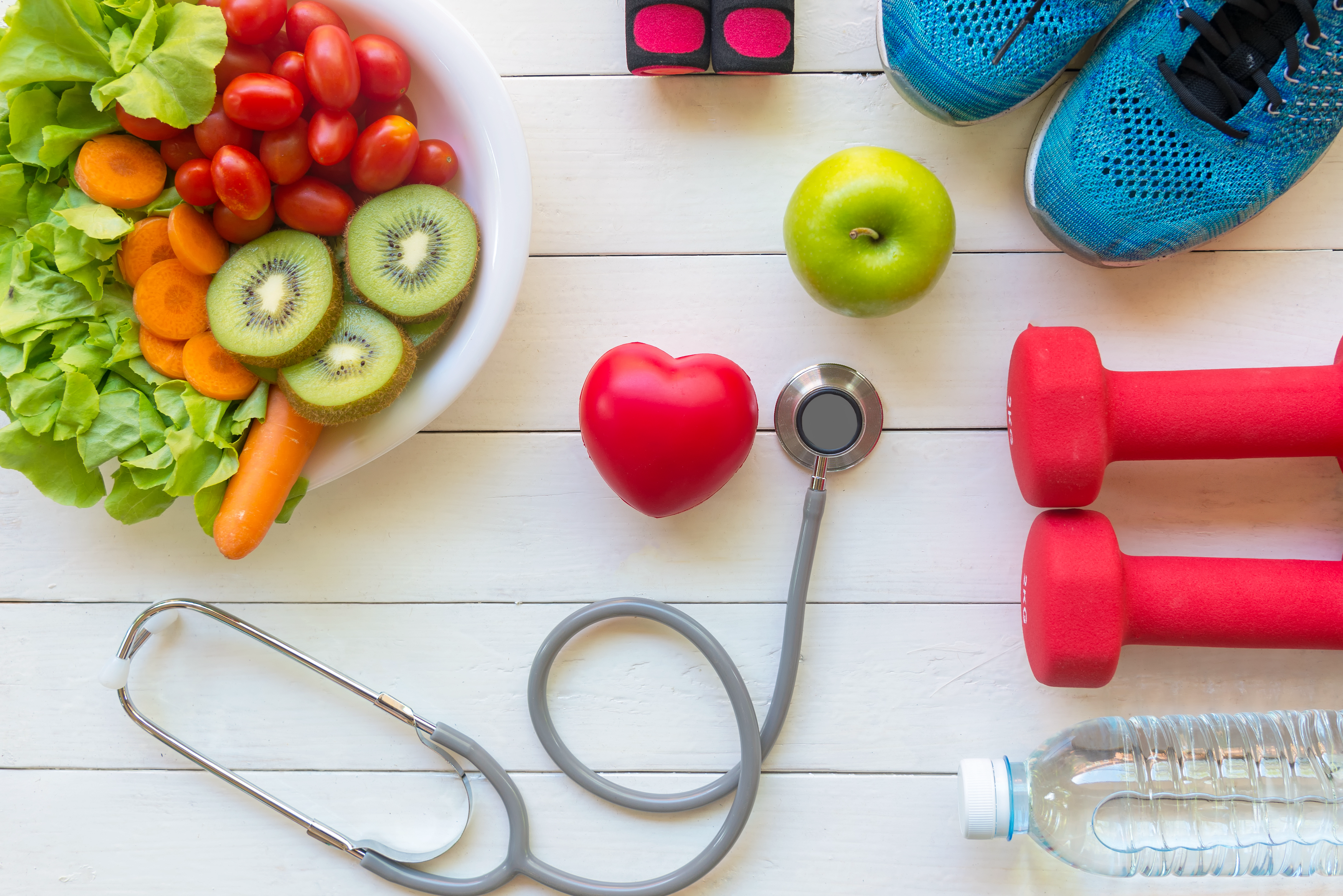 Stethoscope surrounded by vegetables and athletic weights