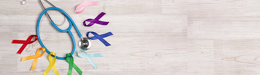 selection of colorful cancer awareness ribbons surrounding a stethoscope on wooden table