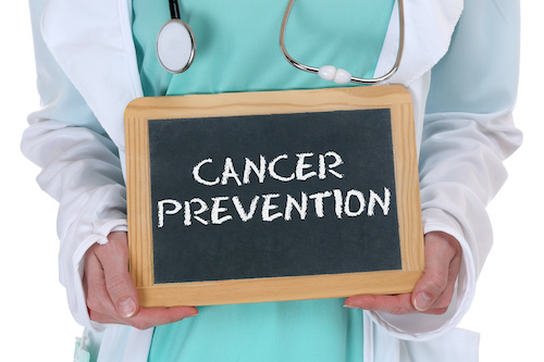 doctor in scrubs and white coat holding a chalkboard with the words cancer prevention written in white chalk