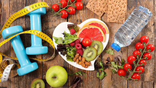 a collection of healthy foods in a heart shaped bowl surrounded by exercise paraphernalia