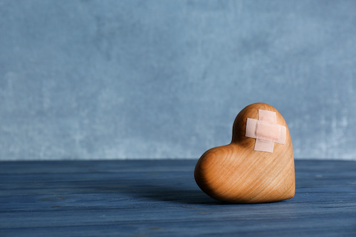 Wooden heart with adhesive plasters on table.