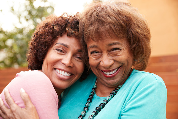Senior black mum and her middle aged daughter smile to camera embracing, close up