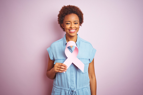 Young african american woman holding brest cancer ribbon over isolated pink background