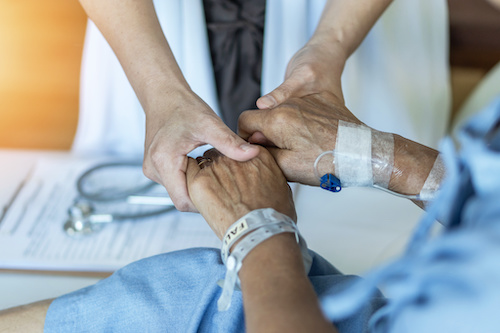 physician holding hands with a patient in a hospital bed