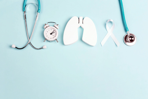 light blue background with white cutout of lungs, white stethoscope, white ribbon, and white clock