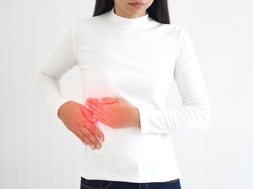 woman in white shirt touching the side of her abdomen