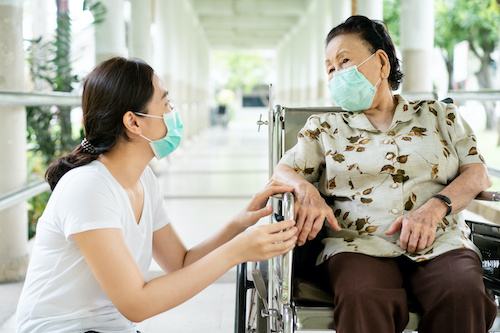 two women in masks, one in wheelchair and one kneeling beside