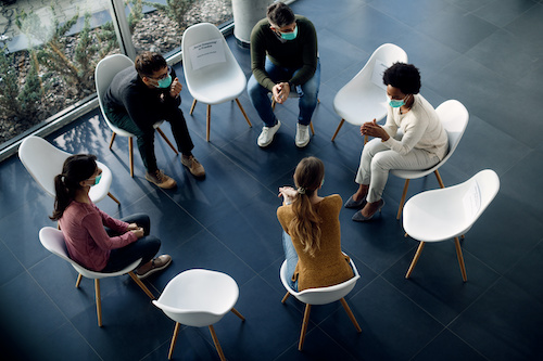 group of adults wearing masks sitting around in circle of chairs