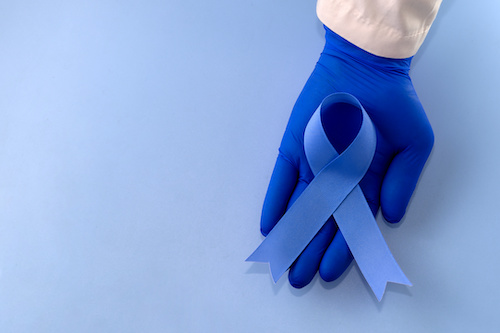 gloved hand holding blue cancer awareness ribbon