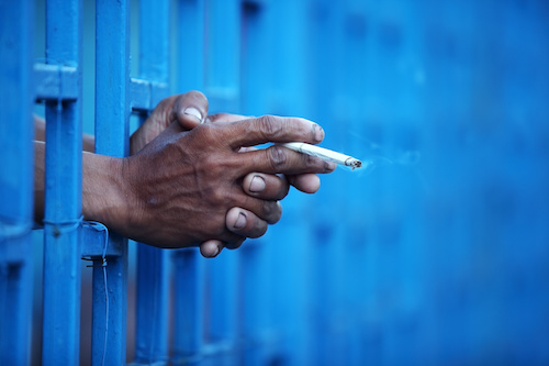 hands reaching through bars holding a cigarette