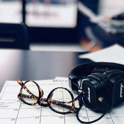 eyeglasses and headphones sitting on top of paper calendar on desk