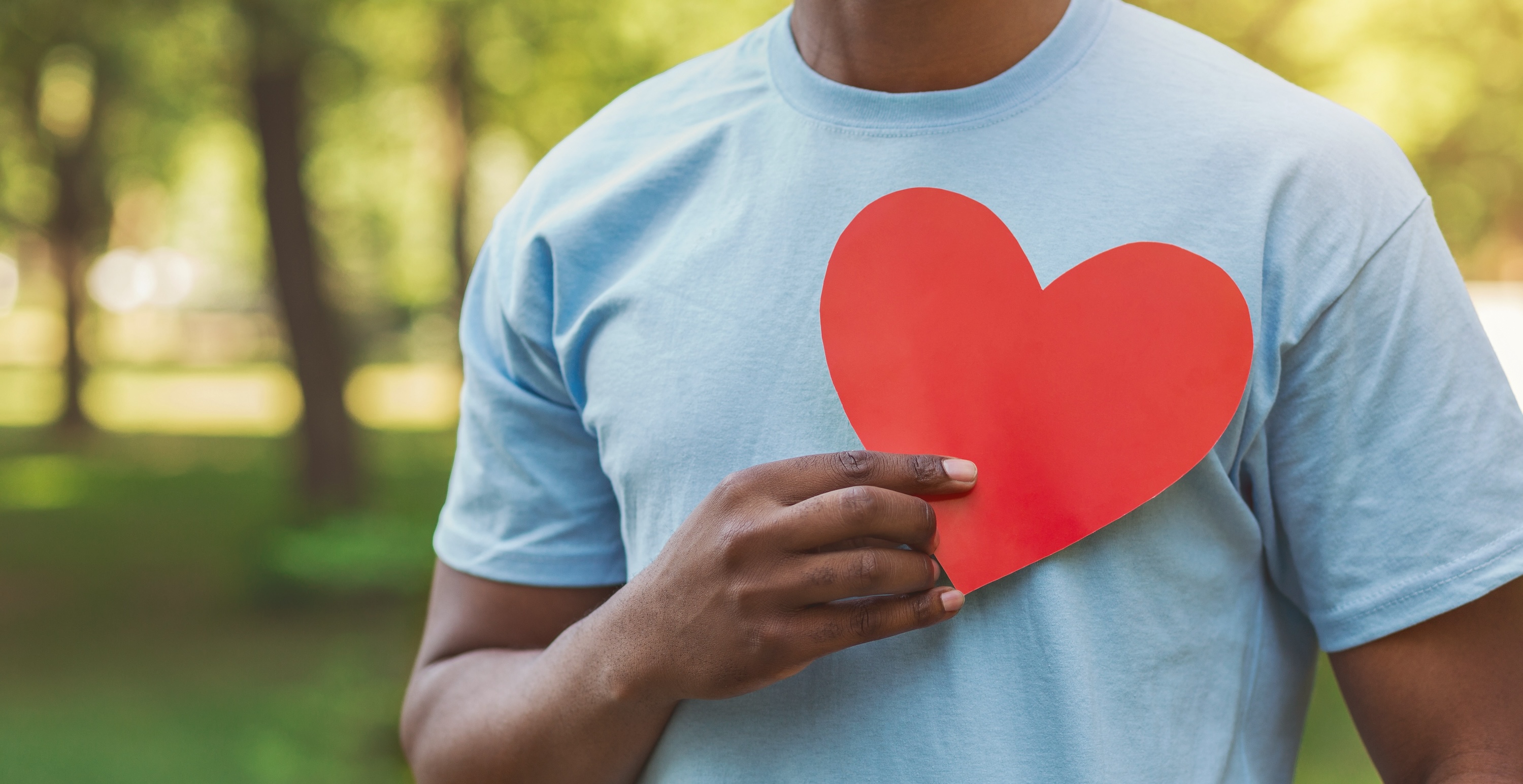 Man in blue tshirt holding red paper heart over his chest