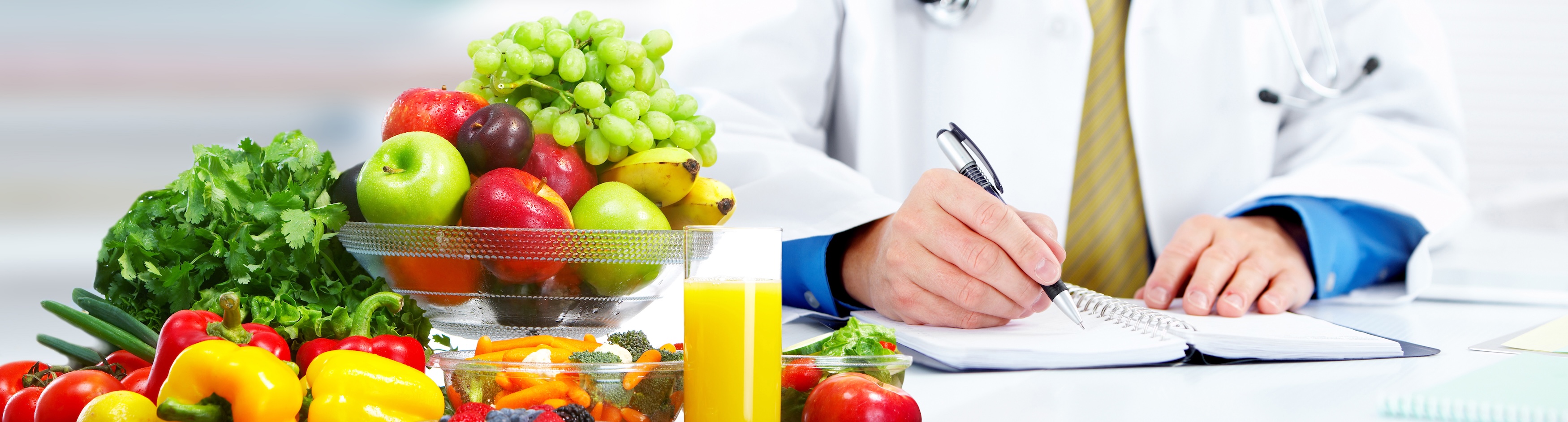 Fruits and vegetables on desk next to doctor writing on clipboard