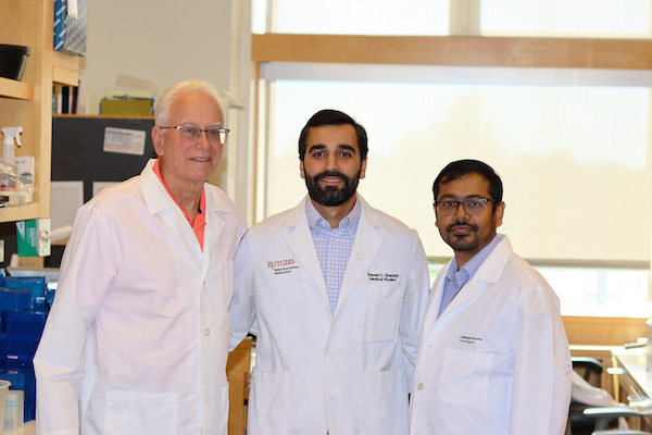 Three men in white lab coats standing in a laboratory environment. From left to right the men are Dr. Blaser, Bassel Ghaddar, and Dr. De