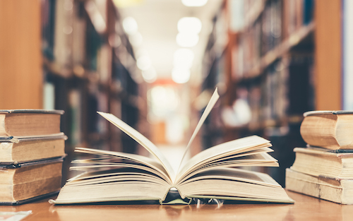 image of open book surrounded by closed books on table in library