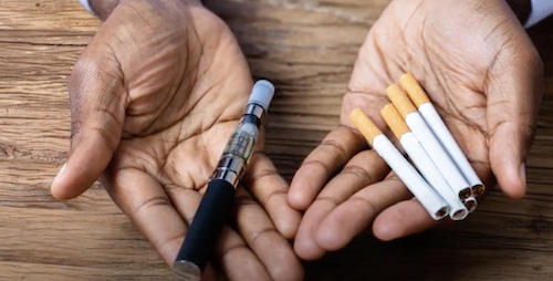 hands holding cigarettes in one hand and a vape in the other