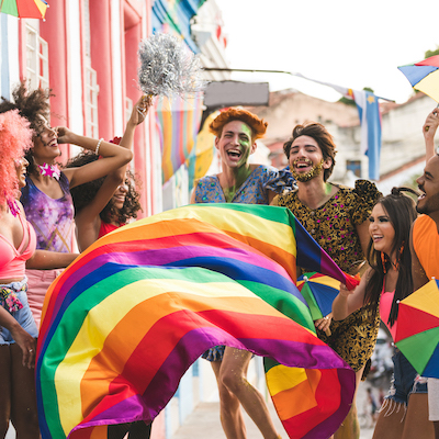 group of young adults dressed for Pride carrying rainbow pride flag