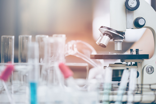 image of microscope on lab bench surrounded by glass test tubes