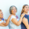 Three generations of smiling Mexican women with blouses with floral patterns in a row holding their shoulders against a white background